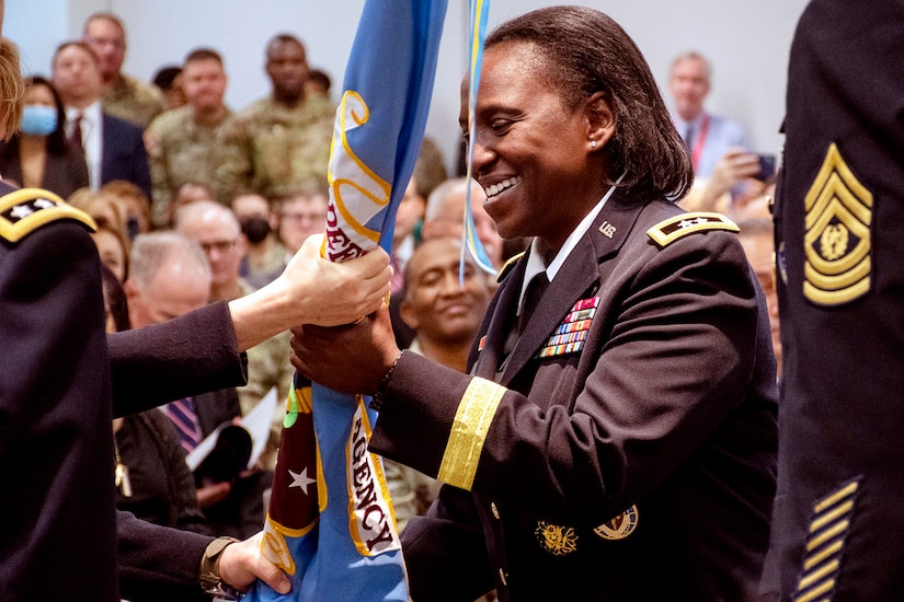 An Army officer smiles and holds a flag during a ceremony.