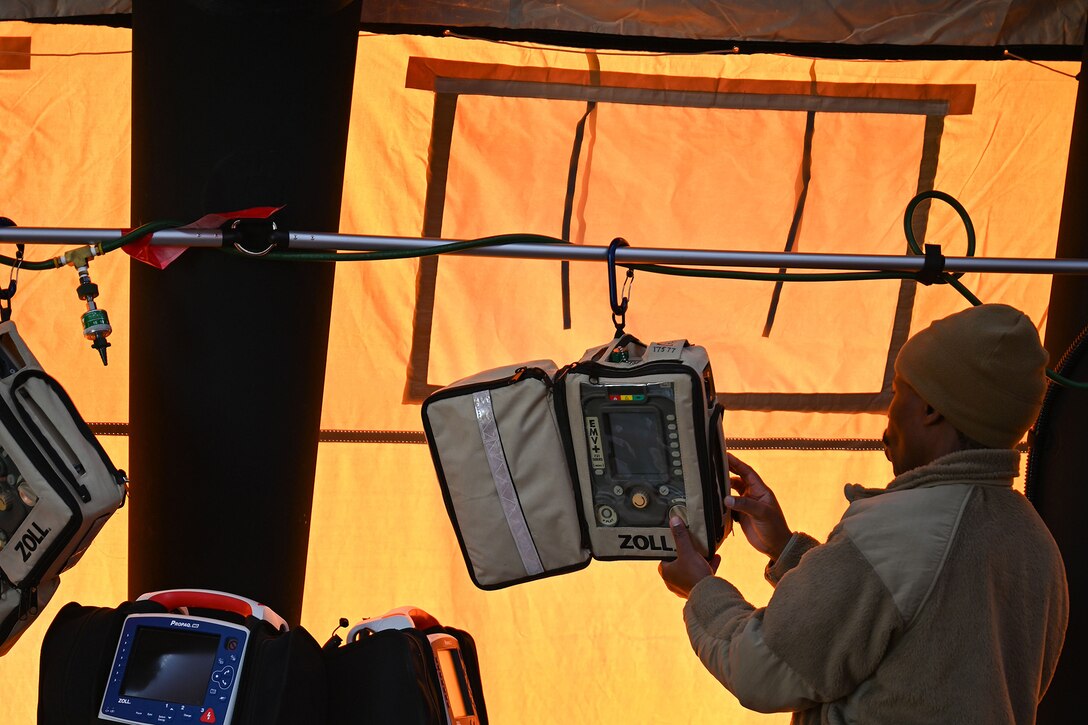 An airman presses a button on a ventilator’s keypad as it hangs from a horizontal pole.