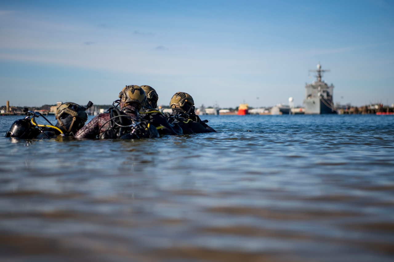 Sailors practice diving skills in a body of water.