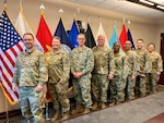 Male and female service members pose in front of the American and military services' flags