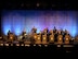 group of men and women wearing u.s. army uniforms sit on a stage and play a variety of musical instruments.