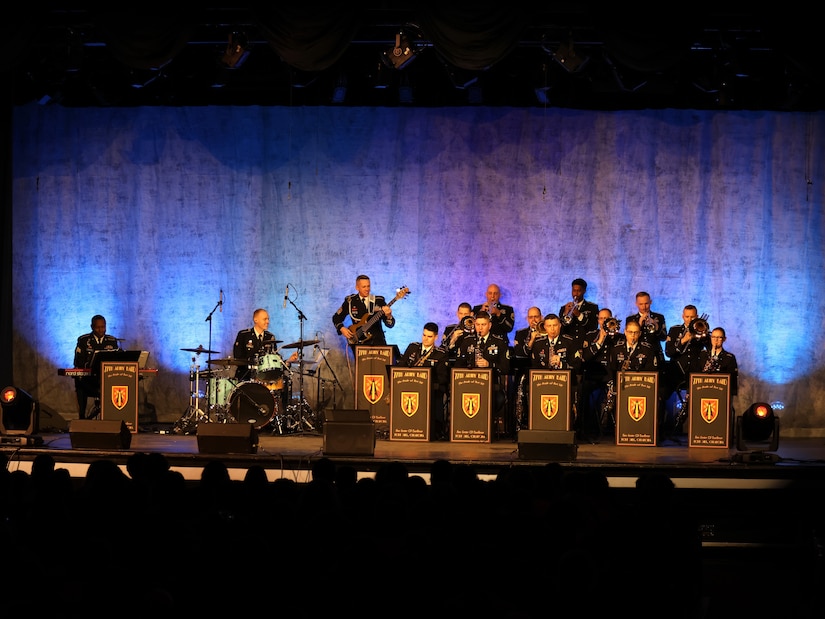 group of men and women wearing u.s. army uniforms sit on a stage and play a variety of musical instruments.