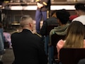 man wearing u.s. army uniform sits next to a female member of the audience and talks.