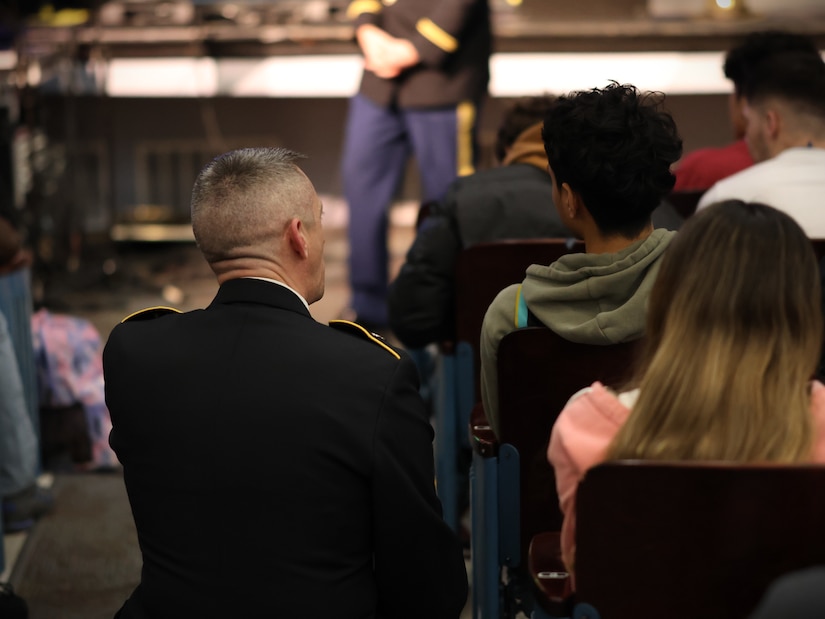 man wearing u.s. army uniform sits next to a female member of the audience and talks.