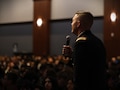 man in u.s. army uniform holds a microphone on a stage.
