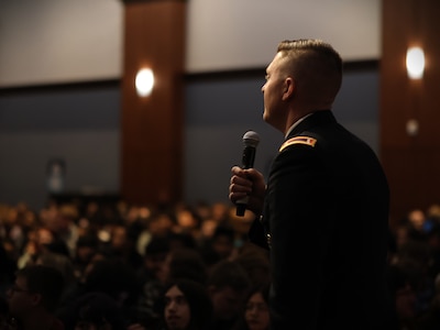 man in u.s. army uniform holds a microphone on a stage.