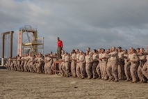 U.S. Marine Corps Staff Sgt. Deandre Lee, a drill instructor with Charlie Company, 1st Recruit Training Battalion, leads warm-up exercises for recruits before they execute a confidence course training event at Marine Corps Recruit Depot San Diego, California, March 11, 2024.  The confidence course is designed to challenge recruits physically and mentally through the execution of obstacles that require strength, balance, and determination. (U.S. Marine Corps photo by Cpl. Sarah M. Grawcock)