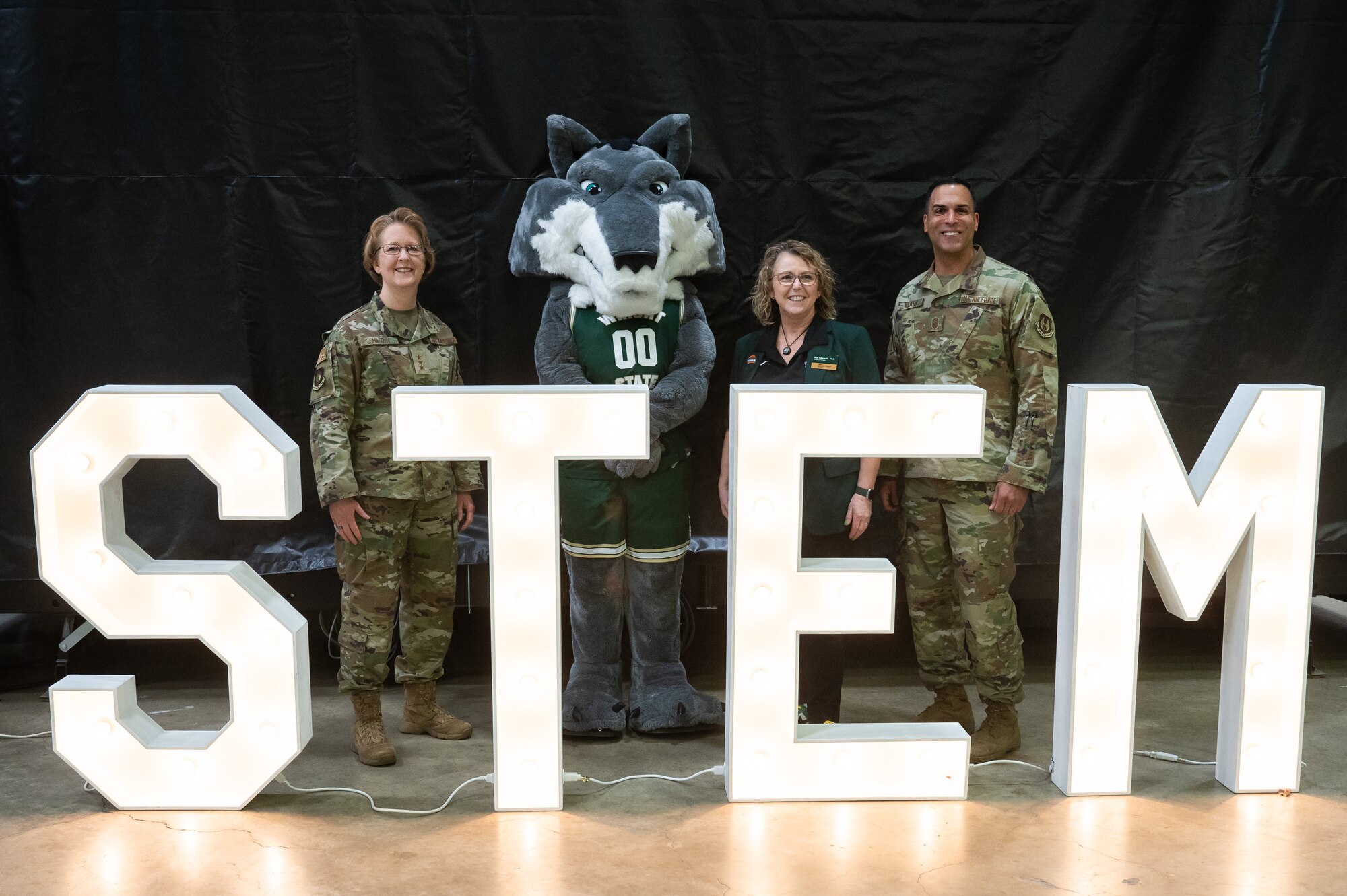 Three adults and WSU mascot stand beside STEM sign.