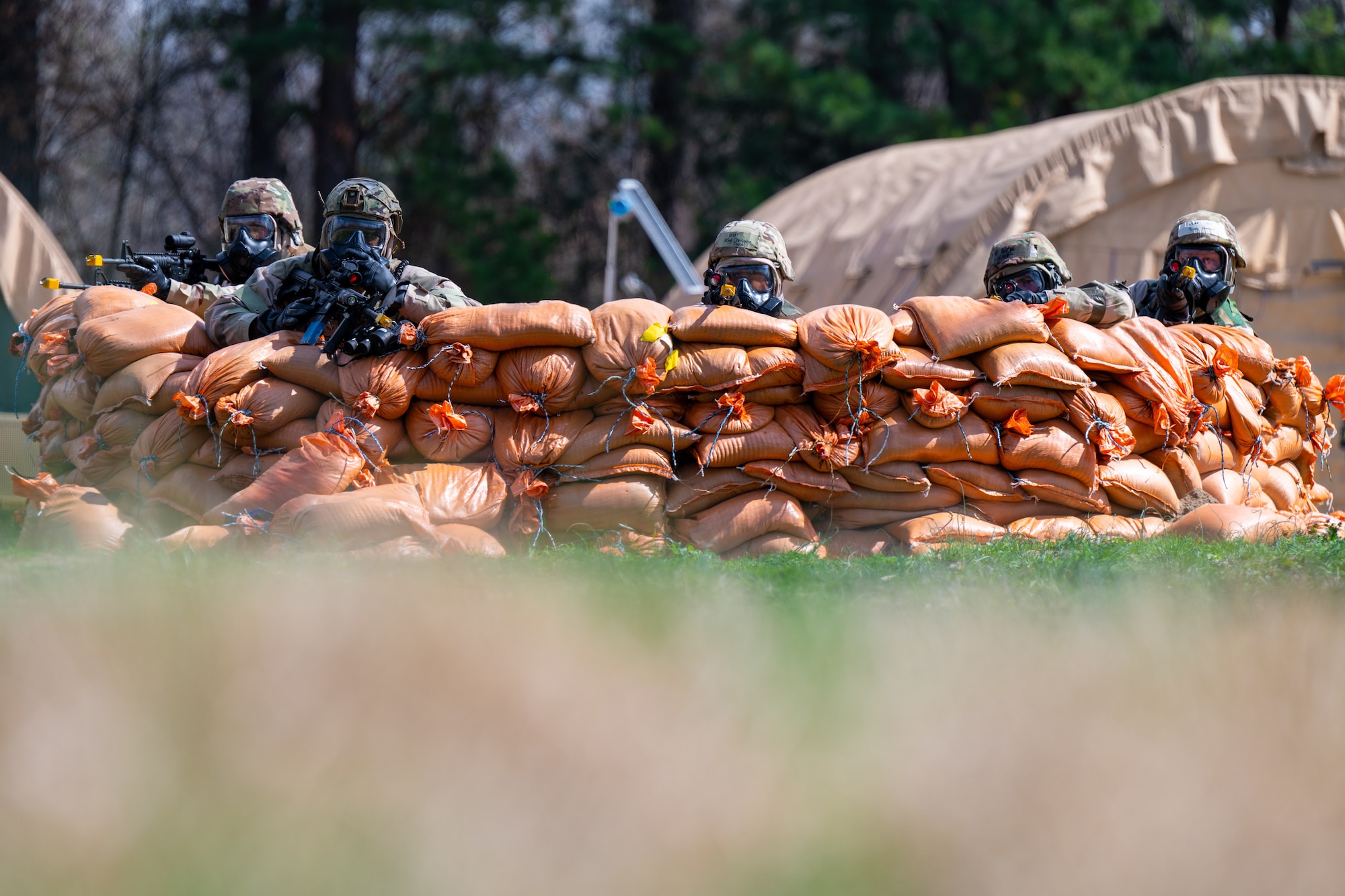 Airmen aim from behind a pile of sandbags.