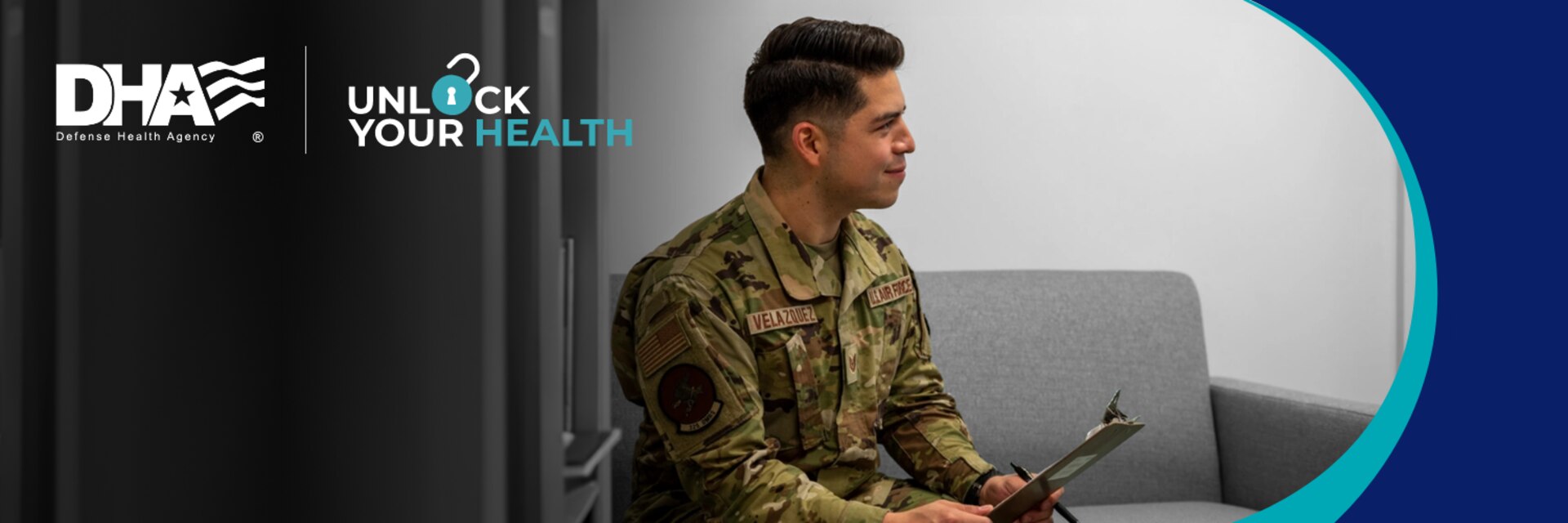 Uniformed Service Member smiles and sits on a couch with clipboard in hand.