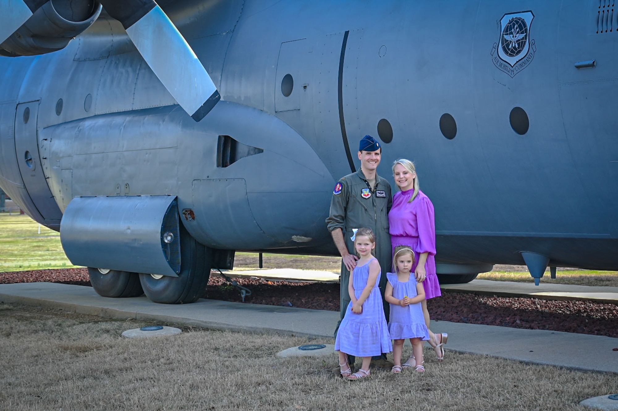 A man and woman pose for a photo with their two children outside next to a aircraft.