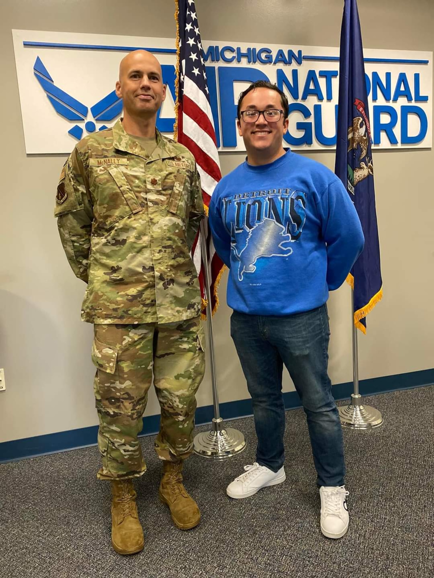 Uniformed Air Force captain poses with civilian in front of Air National Guard sign.