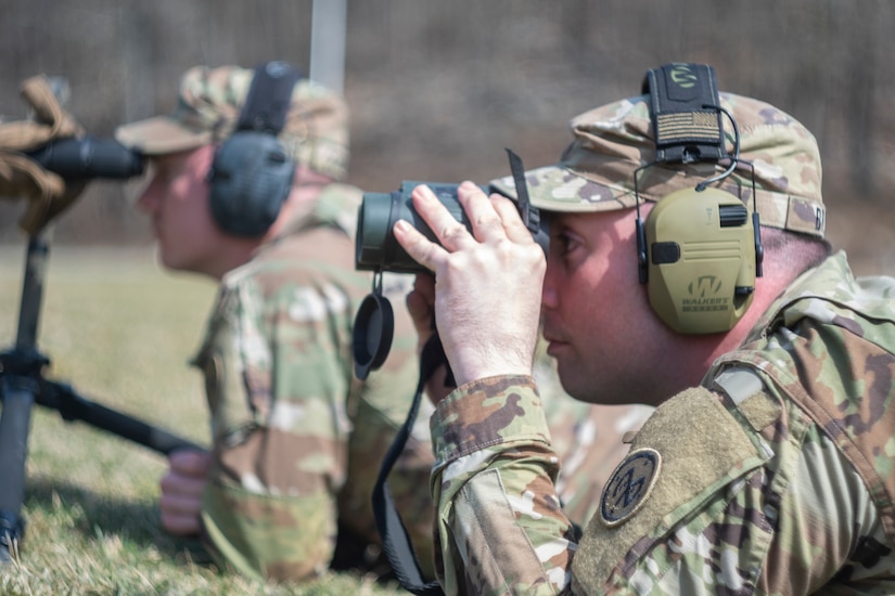 A soldiers uses a pair of binoculars to view a competitor target.