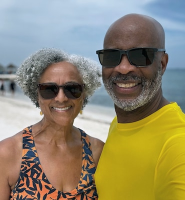 Older black man and woman wearing sunglasses stand on a beach