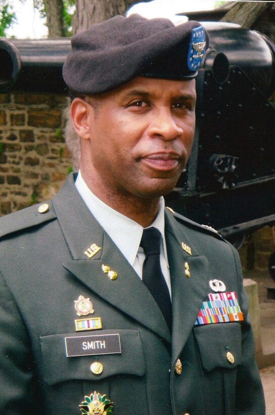 Head and shoulders shot of a black man standing outside in Army green dress uniform and beret.