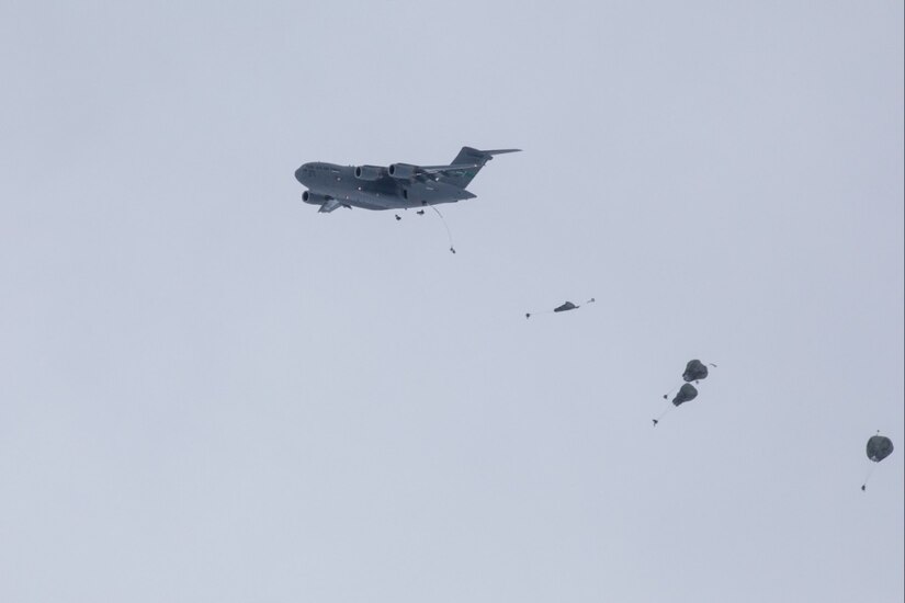 An aircraft flies as soldiers descend with parachutes behind it.