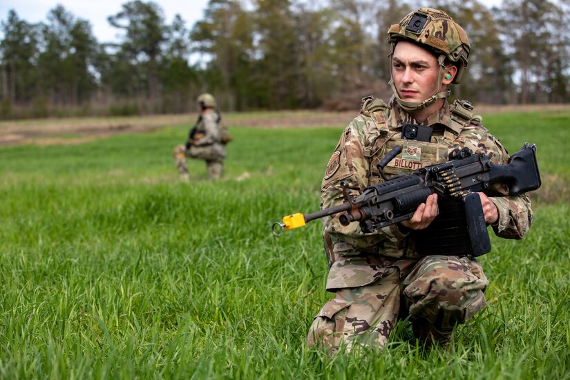 A soldier kneels in grass while holding a weapon.