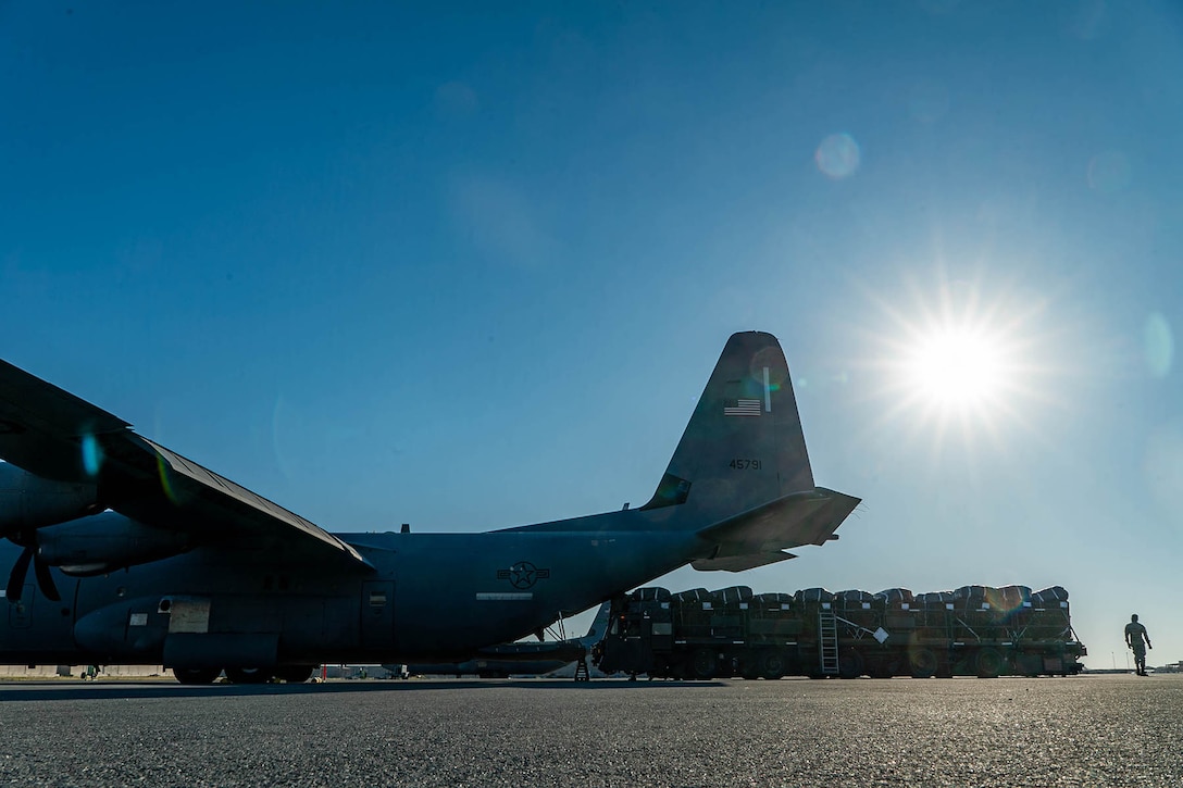 An airman walks near a large pallet by the open rear door of a parked aircraft on a flight line where an airman works.