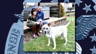 Photo is of a man and woman smiling while looking at a dog.