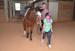 Girl with crutches leading horse.