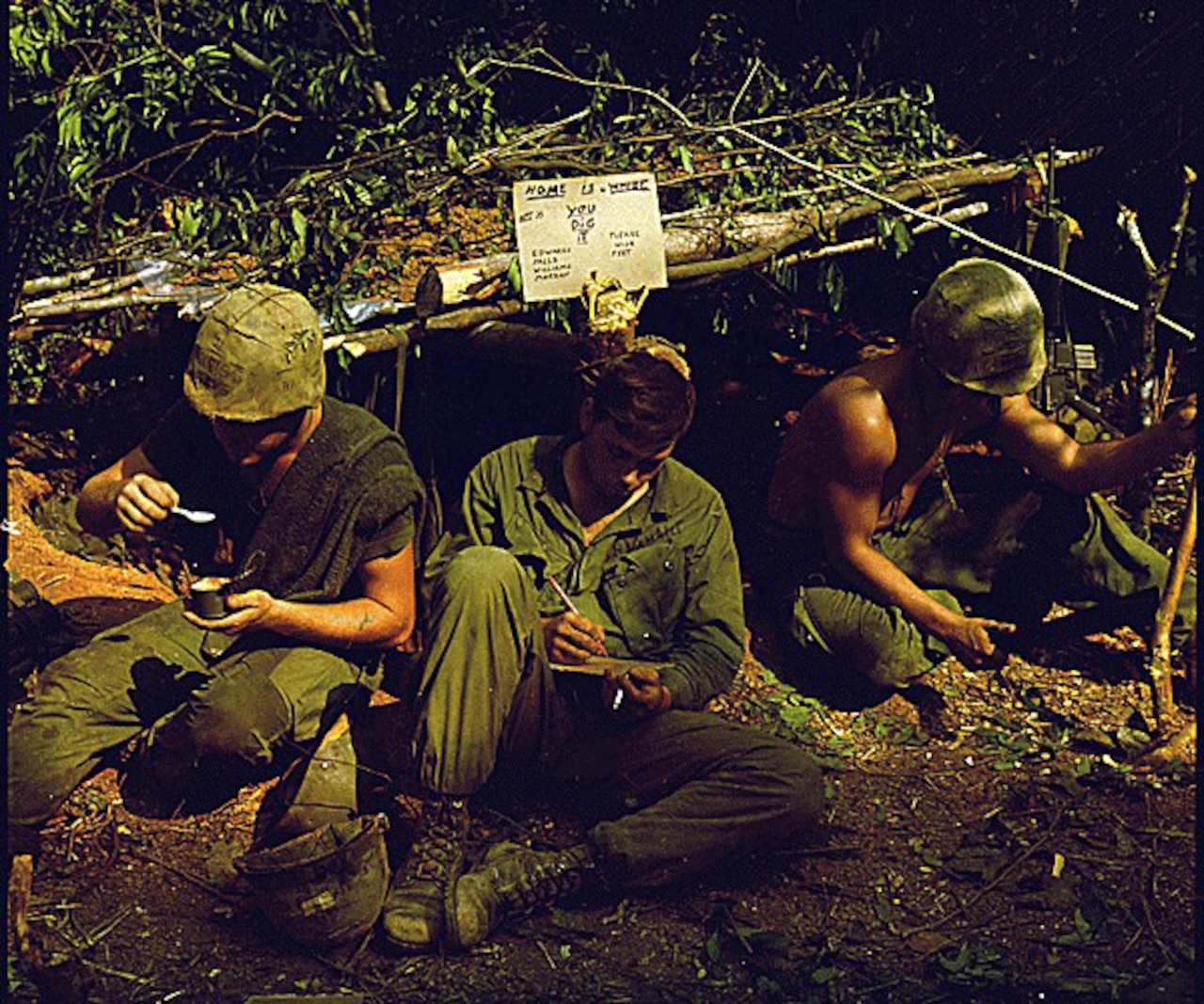 Three men sit on the ground in a makeshift hut.