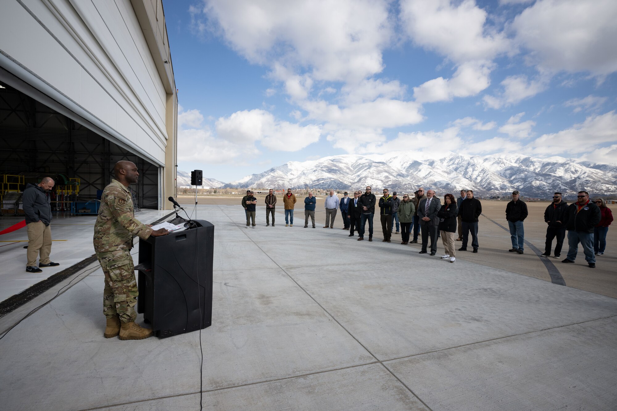 Maj. Gen. Bell addresses guests standing in front of the hangar from behind a podium.