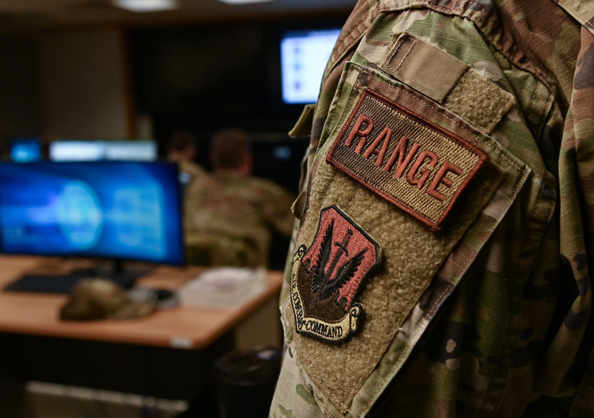 An Airman with a patched titled "Range" stands overlooking a room of computers.