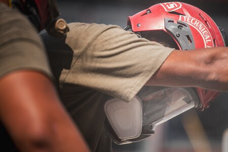 Person in a light brown shirt and red helmet with the word "technical" on the side is leaning forward and looking towards the ground.