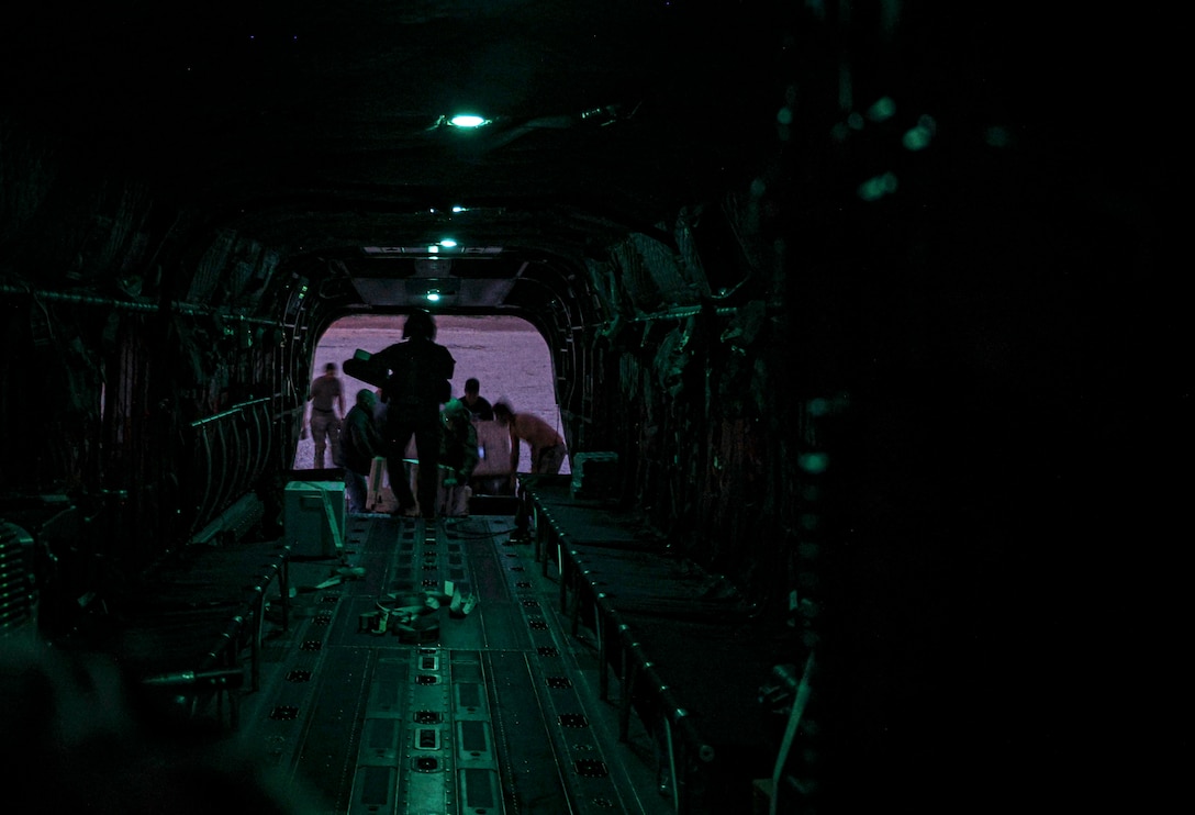 Soldiers walk to the end of a runway on an aircraft that is lowly lit with water below.
