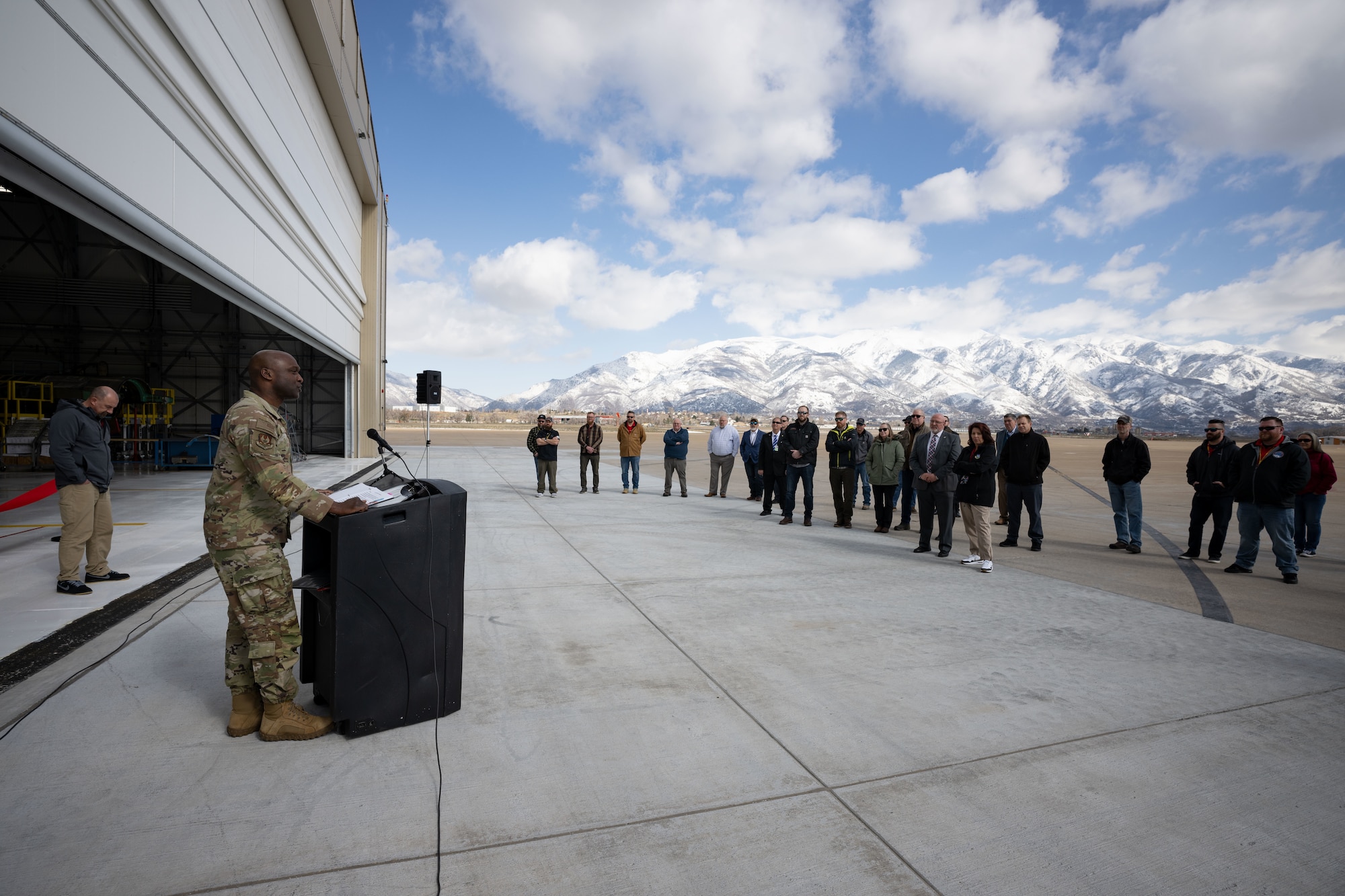 Maj. Gen. Bell addresses guests standing in front of the hangar from behind a podium.