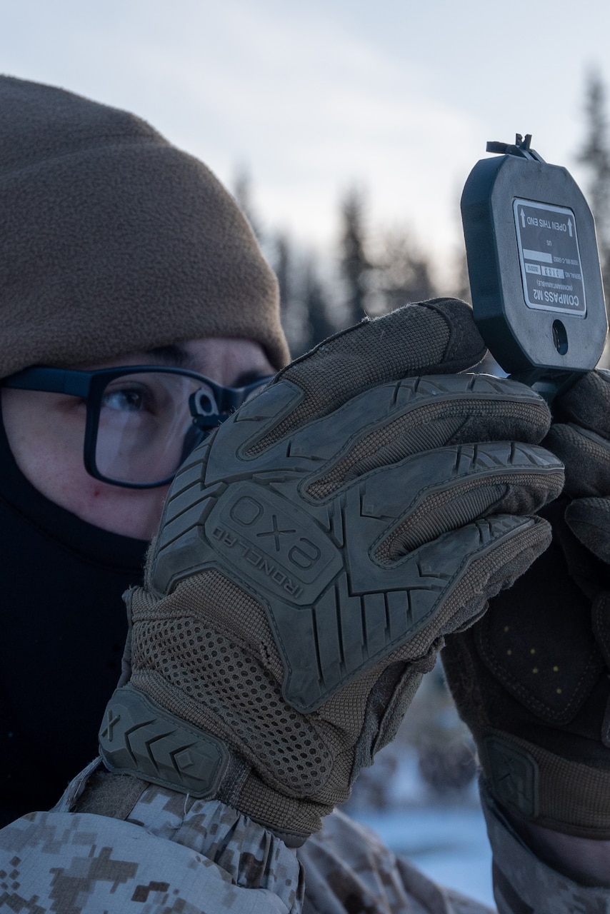 A closeup of a Marine wearing snow gear looking through a device.