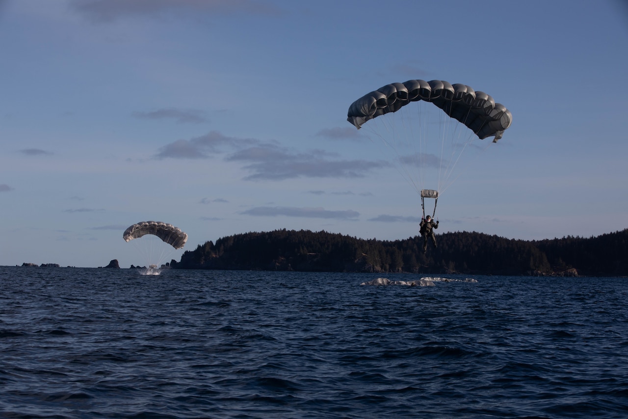 Sailors descend with parachutes into a body of water.
