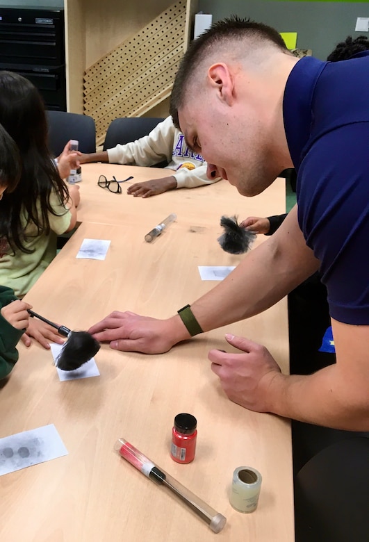 A Special Agent from Army CID instructs School age children how to dust and lift fingerprints.