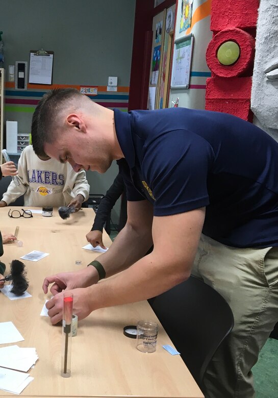 A Special Agent from Army CID instructs School age children how to dust and lift fingerprints.