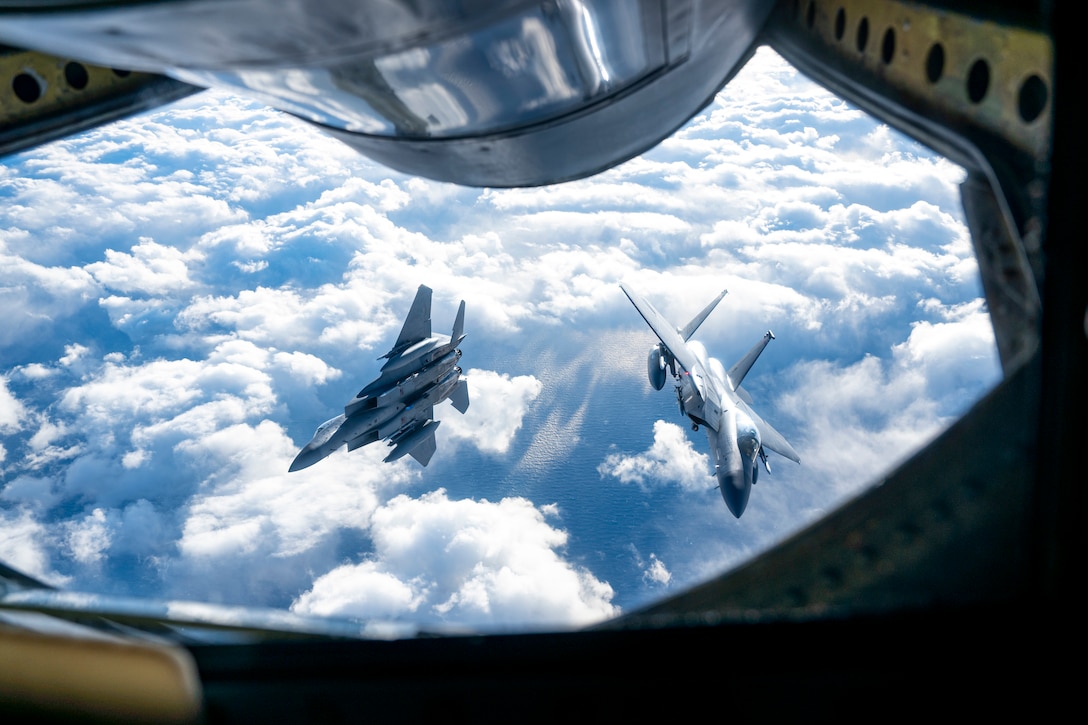 Two fighter jets fly in opposite directions as seen from the refueling window of another aircraft.