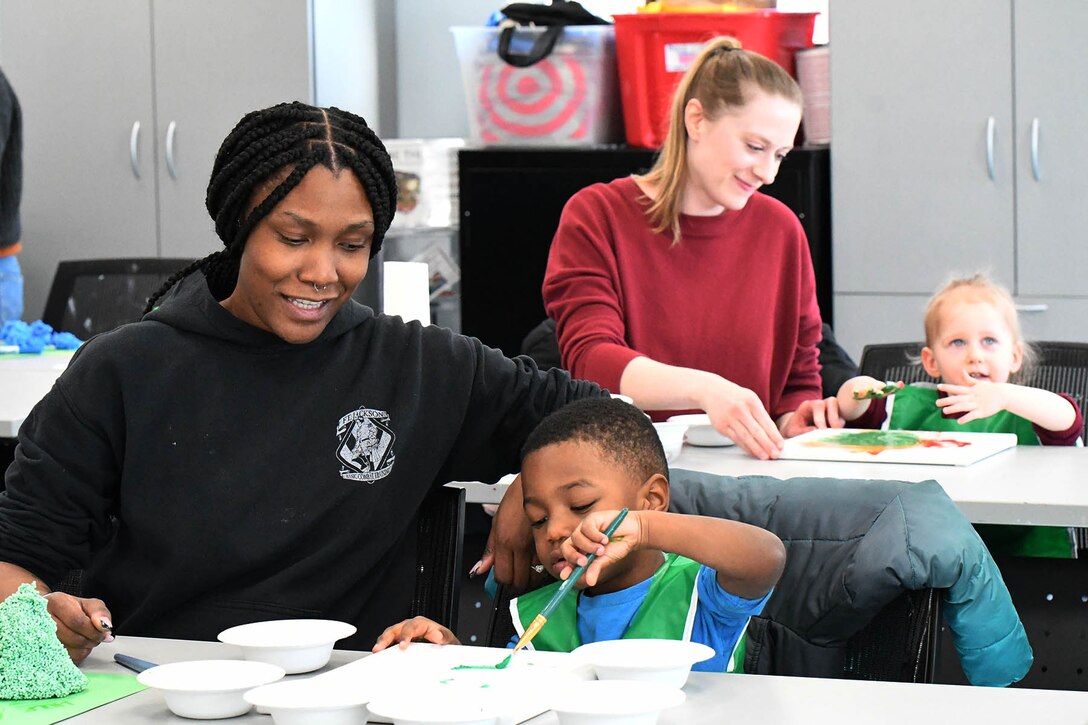 And adult and child paint together at a table as another pair behind them does the same.