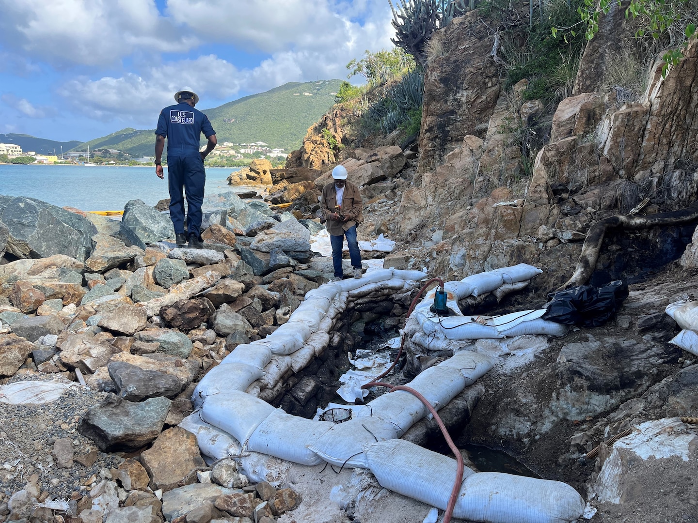A Coast Guard Atlantic Strike Team member and a Virgin Islands Water and Power Authority responder at a collection point at the bottom of natural land veins two and three at Lindbergh Bay from where diesel material is being recovered by clean-up crews in St. Thomas, U.S. Virgin Islands, March 21, 2024. The clean-up site was established following a diesel discharge from the facility's tank 11 that occurred on Oct.25, 2023. (Courtesy photo).