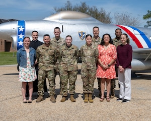 A photo of a group of people posing in front of a stationary air craft.