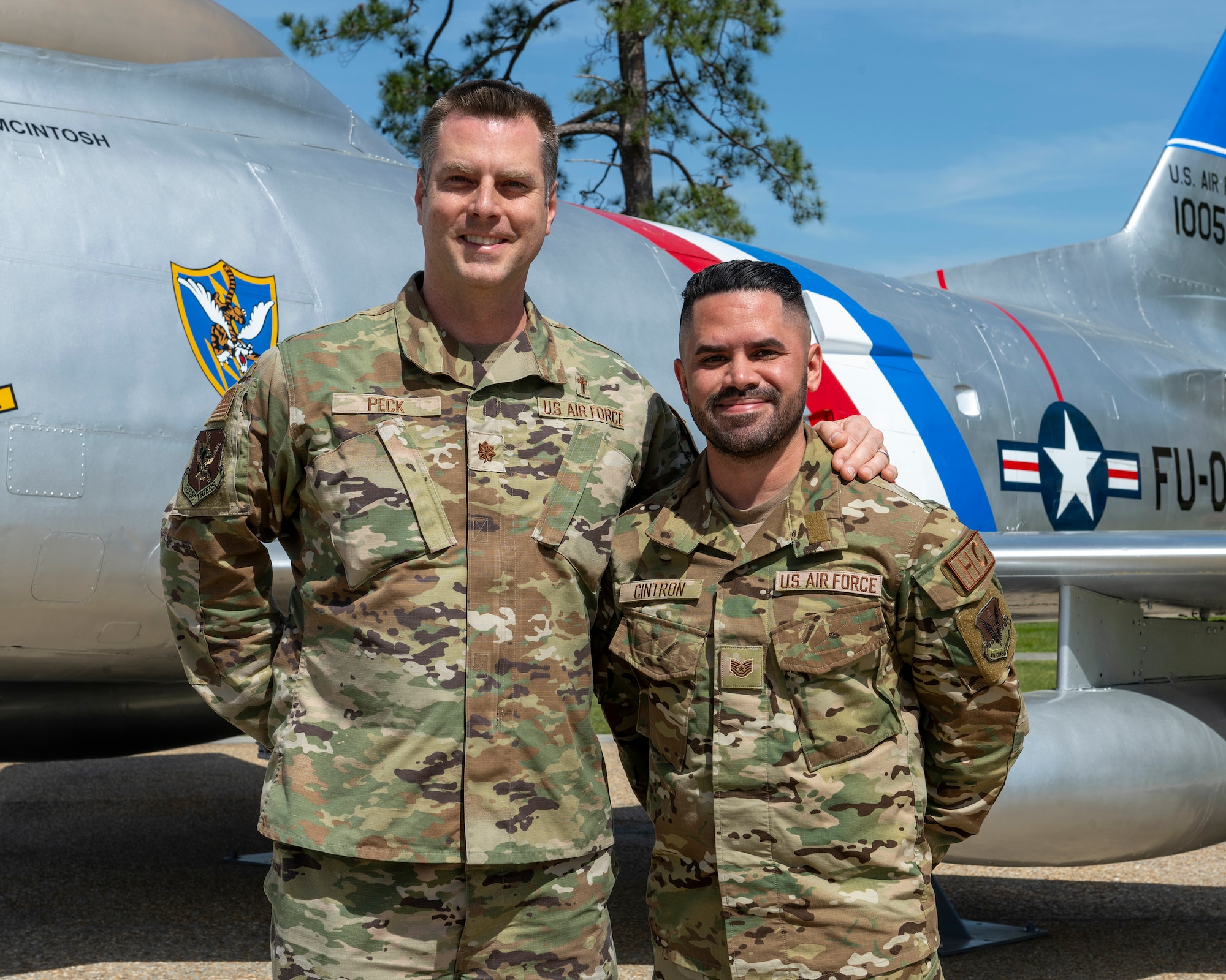 A photo of two people in uniform standing next to each other in front of an aircraft.