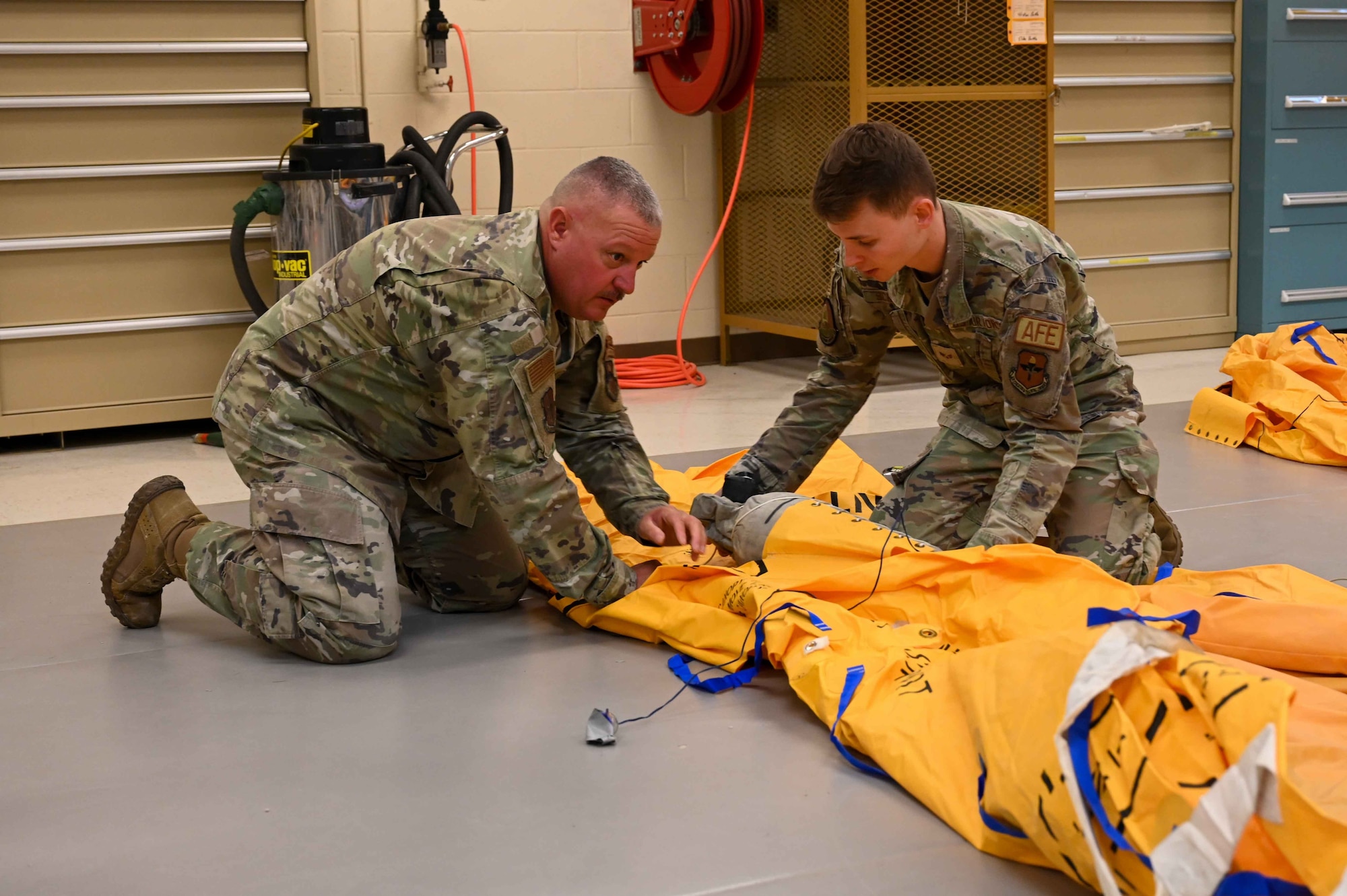 U.S. Air Force Chief Master Sgt. Justin Apticar, left, 19th Air Force command chief, assists Senior Airman Brandon Schulze, right, 97th Operations Support Squadron aircrew flight equipment technician, in rolling up a 46-person raft at Altus Air Force Base (AFB), Oklahoma, March 12, 2024. Apticar toured several squadrons during his two-day visit to interact with Airmen at Altus AFB. (U.S. Air Force photo by Airman 1st Class Kari Degraffenreed)