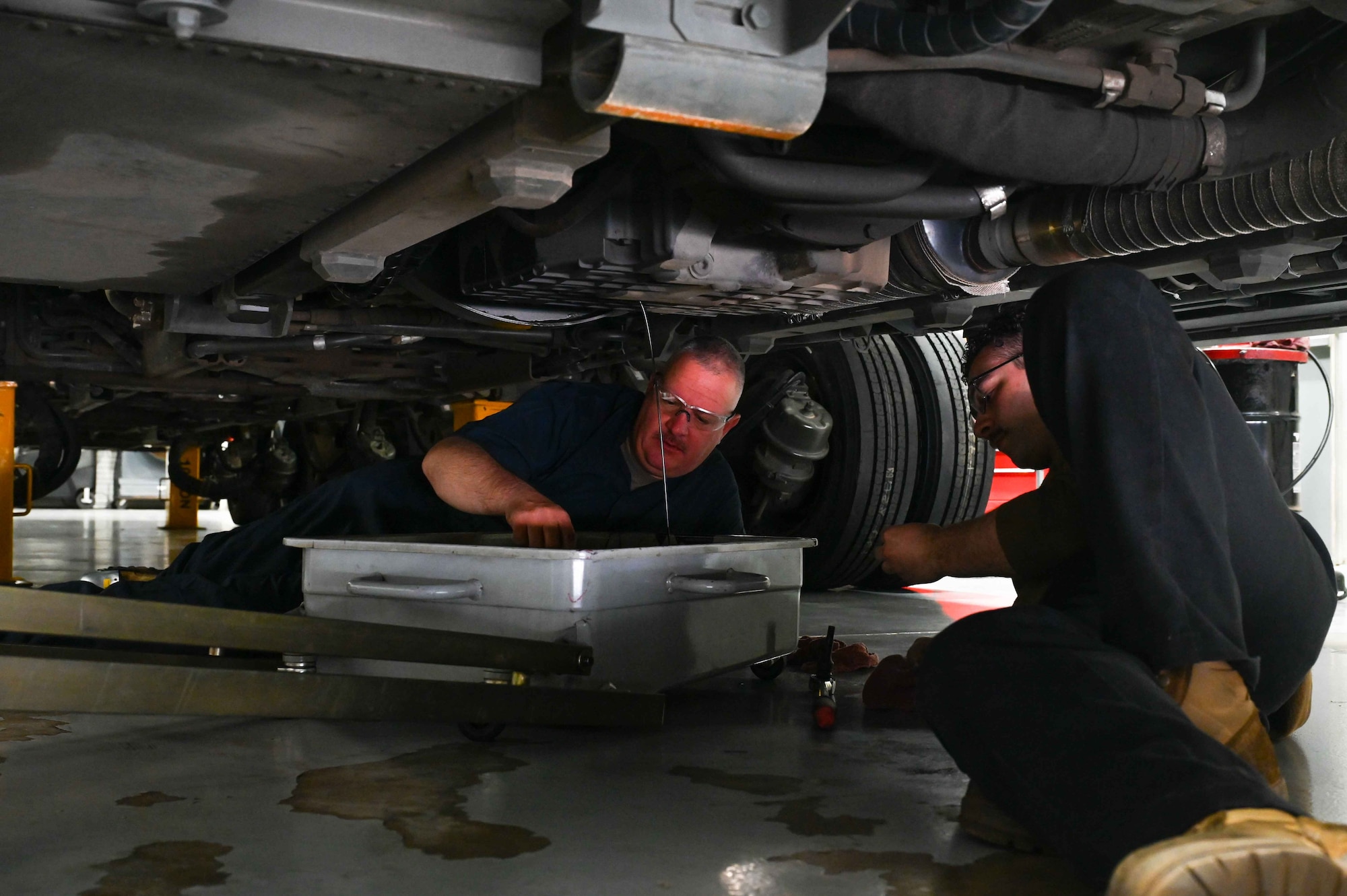 U.S. Air Force Chief Master Sgt. Justin Apticar, left, 19th Air Force command chief, changes the oil on a Tunner 60K Aircraft Cargo Loader/Transporter with Airman 1stClass Logan Gaulin, right, 97th Logistics Readiness Squadron vehicle maintenance technician, at Altus Air Force Base (AFB), Oklahoma, March 13, 2024. While at Altus AFB, Apticar toured the 97th Maintenance Squadron, 97th Medical Group, 97thOperations Support Squadron, and spoke at the Senior Master Sgt. Release Party.(U.S. Air Force photo by Airman 1st Class Kari Degraffenreed)