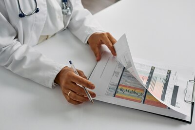 Provider wearing white lab coat flips through papers with charts on clipboard.