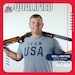 Man in Team USA shirt standing with shotgun.