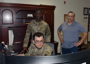 Two men watch another man work on a computer.