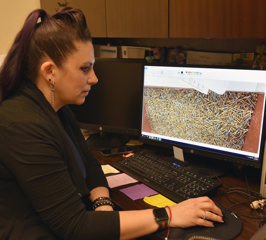 Photo is of a woman sitting at a desk and looking at a computer screen that shows a large amount of nails.