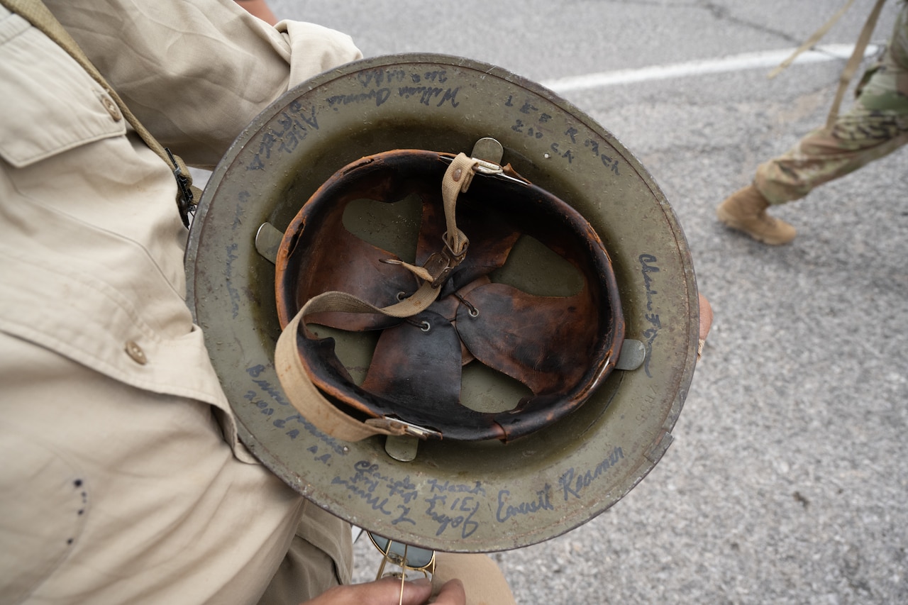 A man displays signatures gathered on the inside of a World War II era helmet worn by foreign service members.