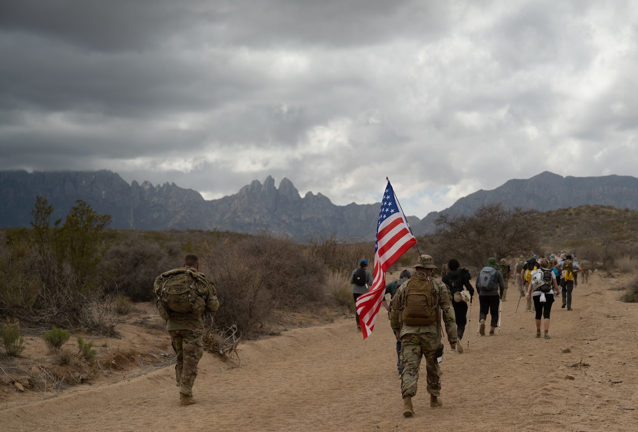A man walks while carrying a backpack with a U.S. flag.