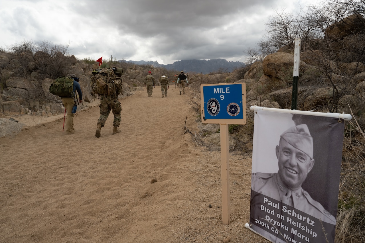 People walk next to a sign displaying a photograph of a World War II veteran.