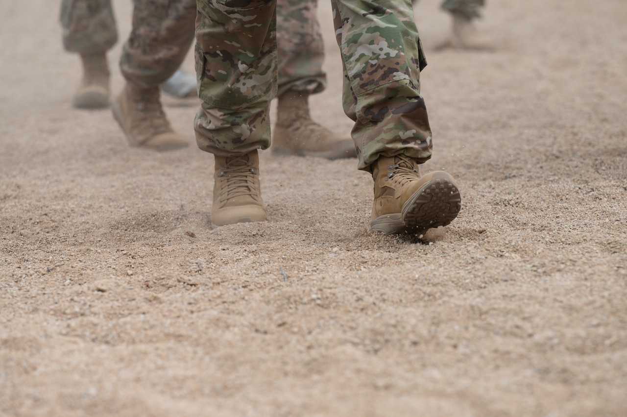 Service members walk through sand.
