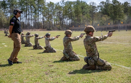 Men in U.S. Army uniforms firing pistols on outdoor pistol range.